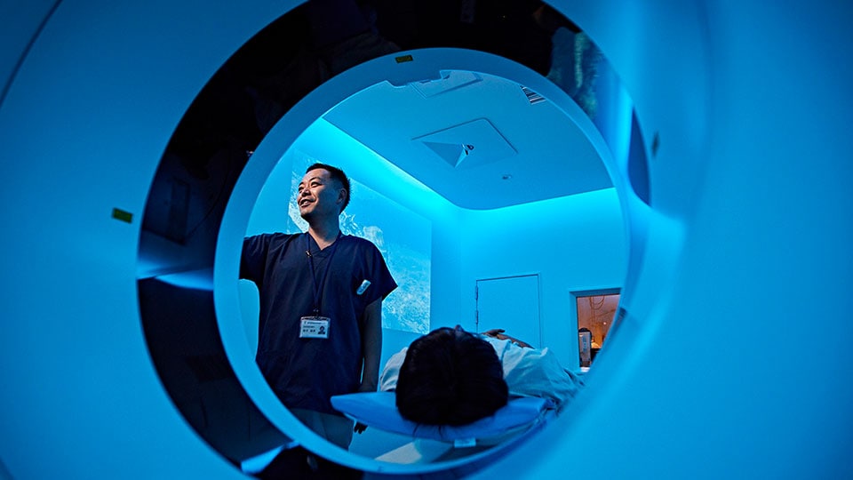 CTシステムの患者テーブルに患者が横たわっており、そこで臨床医がCTスキャナのガントリでスキャンを設定している写真